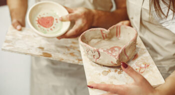 Mutual creative work. Young beautiful couple in casual clothes and aprons. People holds ceramic dishes.